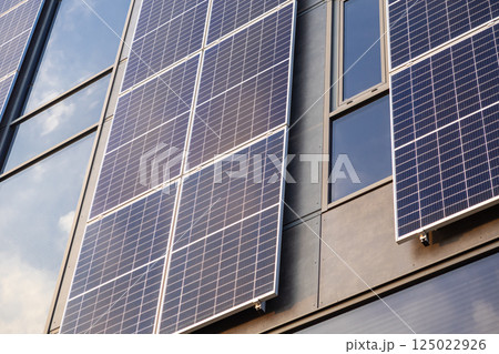 Solar panels installed on modern building facade reflecting sunlight on glass windows during bright clear day 125022926
