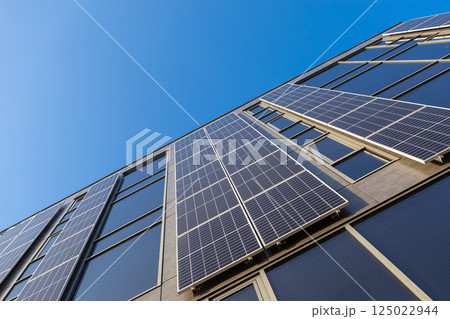 Modern building with installed solar panels on facade for renewable energy and sustainability under clear blue sky low angle view eco friendly architecture Modern building with installed solar panels on facade for renewable energy and sustainability under clear blue sky low angle view eco friendly architecture 125022944