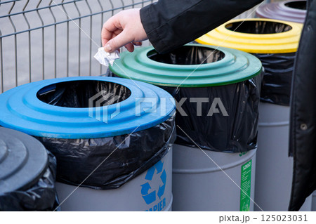 recycling paper into blue bin for eco waste segregation with colorful containers outdoors in public eco-friendly area recycling paper into blue bin for eco waste segregation with colorful containers outdoors in public eco-friendly area 125023031