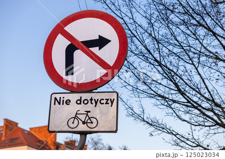 No right turn traffic sign with exception for bicycles on urban street, captured at sunset with tree branches and rooftops in the background 125023034