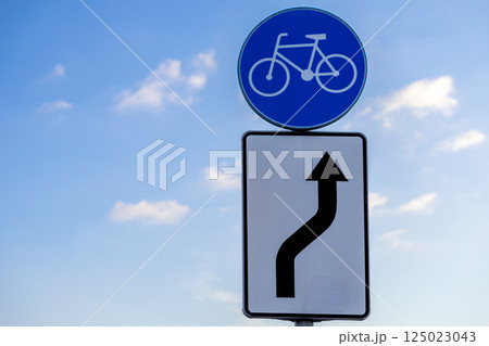 bike path traffic sign and curve direction arrow under blue sky with scattered clouds on sunny day road infrastructure symbol for cyclists navigation bike path traffic sign and curve direction arrow under blue sky with scattered clouds on sunny day road infrastructure symbol for cyclists navigation 125023043
