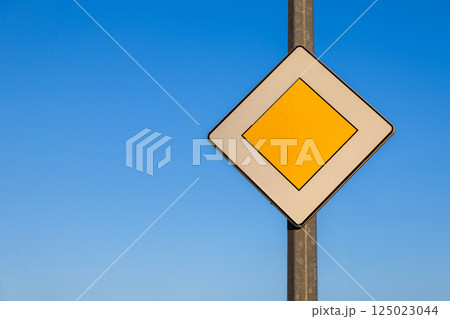 priority road traffic sign with yellow diamond shape on pole against clear blue sky symbolizing main road and traffic regulations on sunny day outdoors 125023044