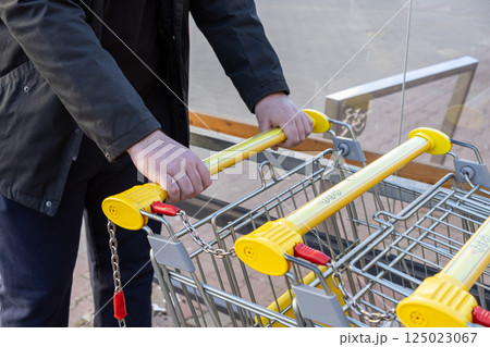 Man unlocking shopping cart with coin at supermarket trolley station with yellow handles and safety chain system on outdoor pavement near glass wall 125023067