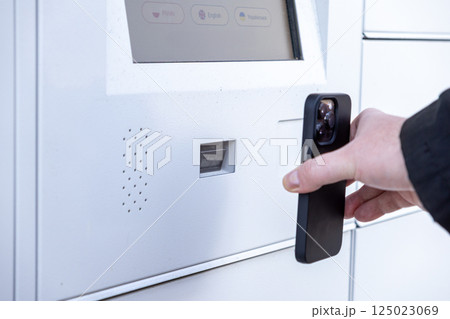 Man scanning smartphone at white parcel locker screen to collect package using QR code or app during modern contactless pickup process 125023069
