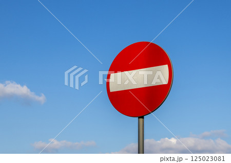 No entry traffic sign with red circle and white bar against blue sky and scattered clouds on a clear sunny day in an urban outdoor setting 125023081