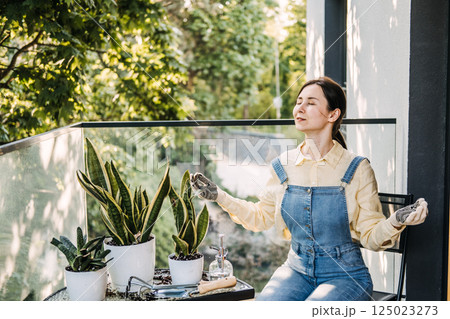 Woman meditating on a balcony with raised arms among potted plants in an urban garden space. Balcony gardening, nature in the city, plant therapy, mindful moments 125023273