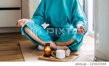 Woman meditating cross-legged near a tray with lit candles and incense on a cork mat. Modern rituals of mindfulness, calming space, grounding practices, self-alignment 125023344