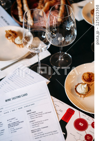 Close-up of a wine tasting card surrounded by dessert plates and glasses on a workshop table. Wine workshop, sensory analysis, food pairing, structured tasting experience 125023368