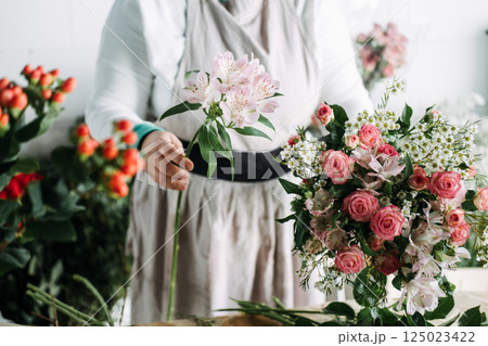 Florist demonstrates bouquet making using pink spray roses and berries during a studio floral class. Floral education and craft classes, hands-on skills, creative learning, bouquet making. 125023422