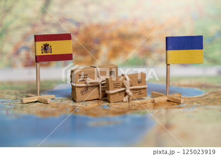 Humanitarian Aid Exchange Between Spain and Ukraine Symbolized by National Flags and Parcels on World Map 125023919