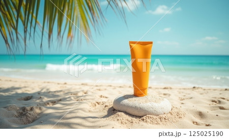 Orange sunscreen tube on white stone at sandy tropical beach with ocean waves and palm leaves. Mockup for skincare and sun protection products, copy space 125025190