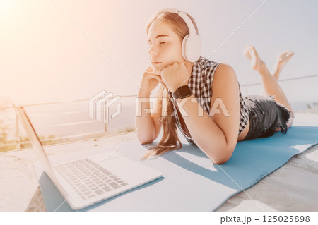 Young Woman Relaxing on the Beach, Listening to Music, and Using Laptop 125025898