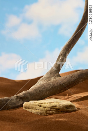 Trunk of an ancient tree with branches is dark brown, dented in places and has light wood grain. The rough rock is worn away by time and buried in sand. Blue sky background with white clouds 125026992