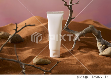 Frontal shot of an unlabeled tube in a desert landscape with dry branches all around. Dry sand covers rough pebbles. Winding tree trunks are withered by the sun. Sand dunes rise and fall in behind.  125027017