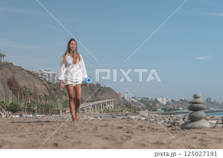 Woman walking on beach holding yoga mat in summer Woman walking on beach holding yoga mat in summer 125027191
