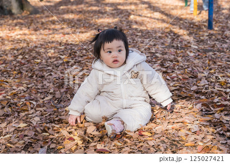【落ち葉で敷き詰められた冬の公園で遊ぶ1歳児　座る】 125027421