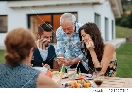 Older man showing photos on smartphone during spring family barbecue. 125027543