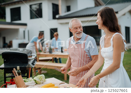 Older father and adult daughter preparing food for a family barbecue. Older father and adult daughter preparing food for a family barbecue. 125027601
