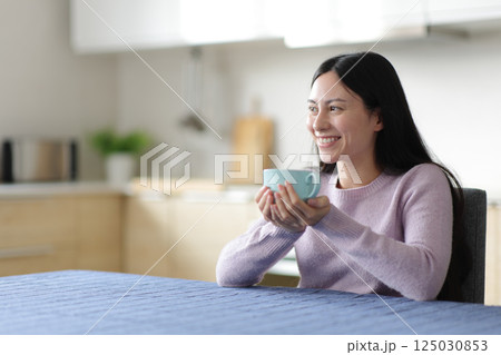 Asian woman drinking tea looking away at home Asian woman drinking tea looking away at home 125030853