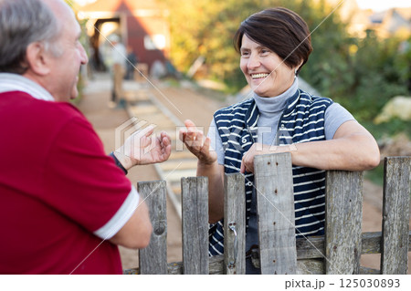 Elderly couple standing together near wooden fence in garden Elderly couple standing together near wooden fence in garden 125030893