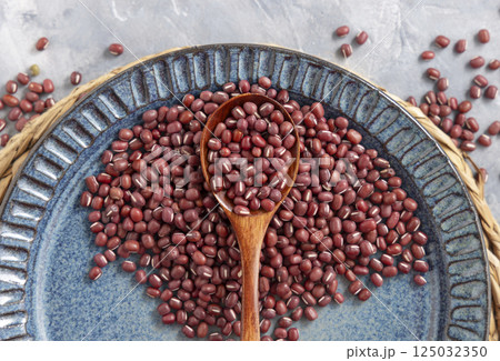 Blue plate full of dried red azuki beans with a wooden spoon top view. Vegetarian protein source 125032350