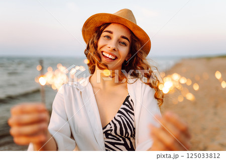 The sparklers in hands of young woman on the beach. Woman enjoying party on beach with sparklers. The sparklers in hands of young woman on the beach. Woman enjoying party on beach with sparklers. 125033812