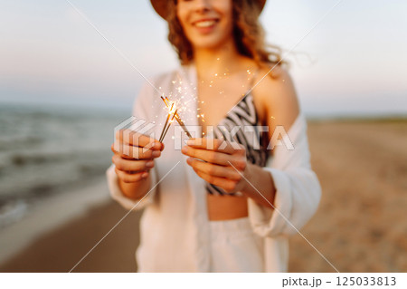 The sparklers in hands of young woman on the beach. Woman enjoying party on beach with sparklers. 125033813