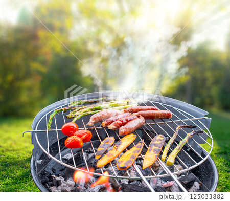 close-up top view of a charcoal grill with sausages, asparagus and cherry tomatoes being grilled outdoors at backyard 125033882