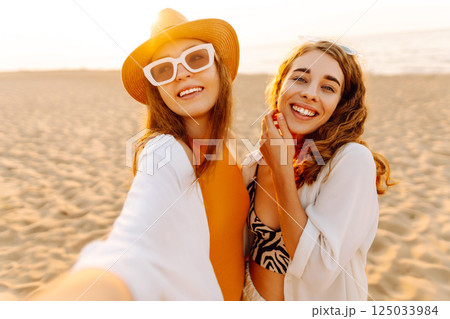 Two pretty friends women making selfie on beach, light and bright summer colors. Friends together 125033984