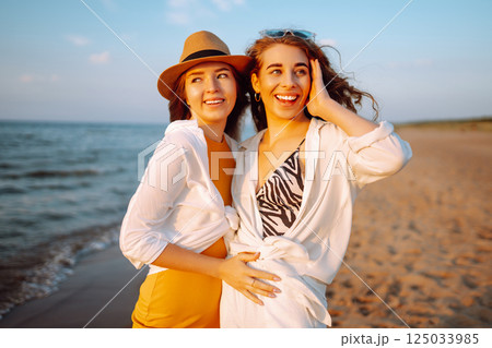Portrait of two young female friends walking on the sea shore at sunset. Lifestyle concept. 125033985