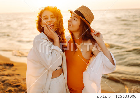 Portrait of two young female friends walking on the sea shore at sunset. Lifestyle concept. 125033986