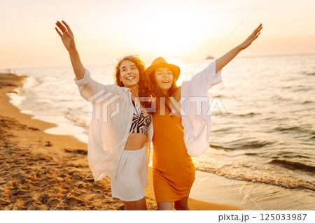 Portrait of two young female friends walking on the sea shore at sunset. Lifestyle concept. Portrait of two young female friends walking on the sea shore at sunset. Lifestyle concept. 125033987