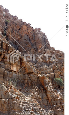Dark red cliffs reveal angular rock surfaces, orange cracks run sharply down, split blocks create deep vertical lines, diagonal erosion cuts show ancient pressure movement. Angular compression concept Dark red cliffs reveal angular rock surfaces, orange cracks run sharply down, split blocks create deep vertical lines, diagonal erosion cuts show ancient pressure movement. Angular compression concept 125034128