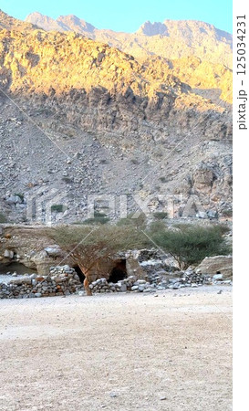 Historical village with natural caves nestled in rocky mountains. Stone structures blend with harsh terrain, echoing remnants of early civilization. Remote setting preserves cultural past. 125034231
