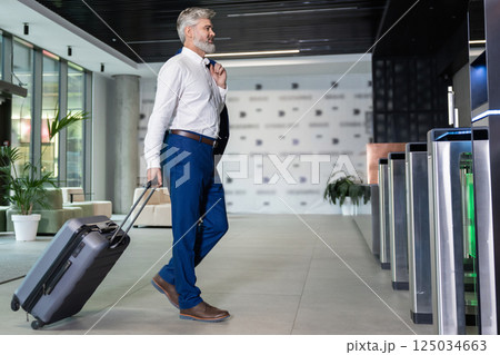 Bearded man walking in airport terminal carrying suitcase 125034663