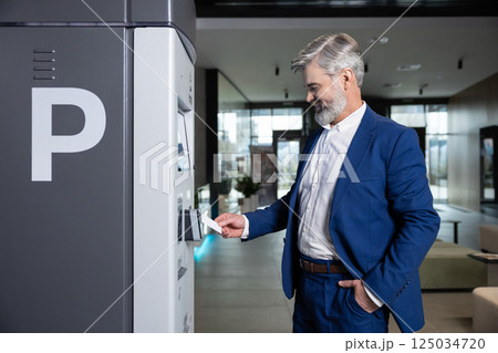 Male using electronic system at parking facility to buy ticket in automotive station 125034720
