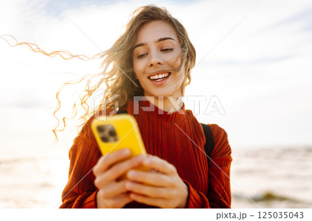 Young woman using mobile phone at beach. Cold weather. Autumn. Blogging, communication 125035043