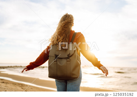 As she walked along the beach, the woman tourist adjusted her backpack, taking in the salty sea air 125035192