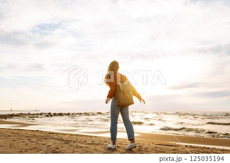 As she walked along the beach, the woman tourist adjusted her backpack, taking in the salty sea air 125035194