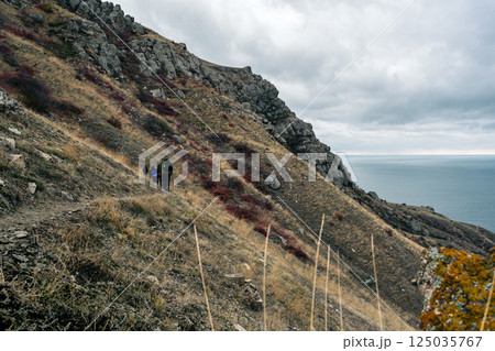 Hikers navigate rocky terrain along a coastal path under overcast skies in a remote landscape 125035767