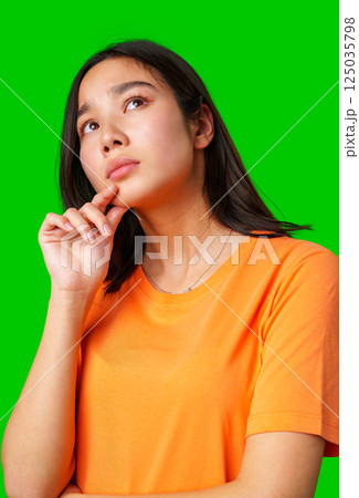 Young woman in orange shirt contemplating against bright green background during creative photoshoot 125035798