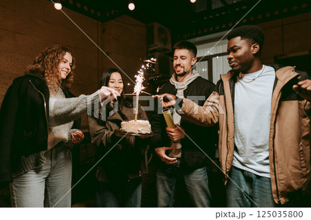Friends celebrate birthday with cake and sparklers in cozy indoor setting 125035800