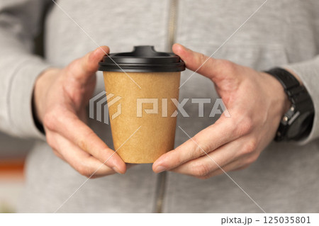 Man's hands holding a craft disposable paper cup with fresh coffee. 125035801