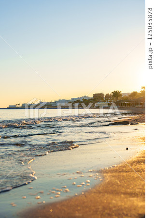 Sunset over a tranquil beach with gentle waves lapping against the golden sand in a coastal town Sunset over a tranquil beach with gentle waves lapping against the golden sand in a coastal town 125035878