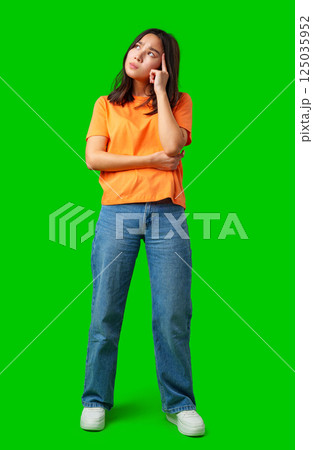 Young woman in casual attire deep in thought against a bright green background during a creative brainstorming session 125035952