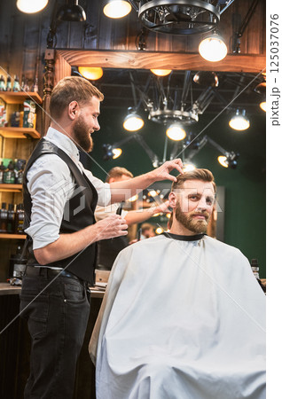 Hairdresser making final touches in new haircut. Comfortable atmosphere in modern barbershop. Hairdresser making final touches in new haircut. Comfortable atmosphere in modern barbershop. 125037076
