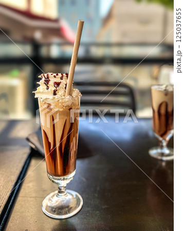 Iced coffee with whipped cream and chocolate on the table in cafe with bokeh background 125037655