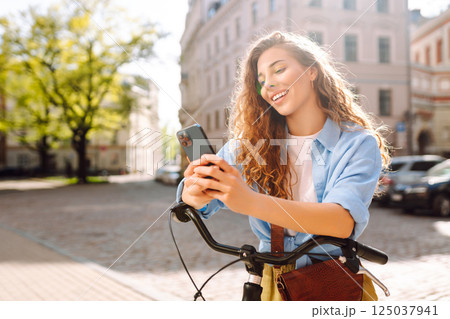 Young woman using mobile phone while riding bicycle at the city street outdoor. Selfie time. 125037941