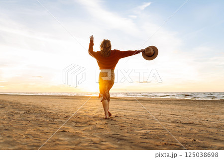 Stylish woman walks at sunset along beach of sea on at sunset. Travel, relax and lifestyle concept. 125038698
