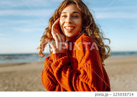 Portrait of curly woman on beach in cold sunny weather. Travel, weekend, relax and lifestyle concept Portrait of curly woman on beach in cold sunny weather. Travel, weekend, relax and lifestyle concept 125038714